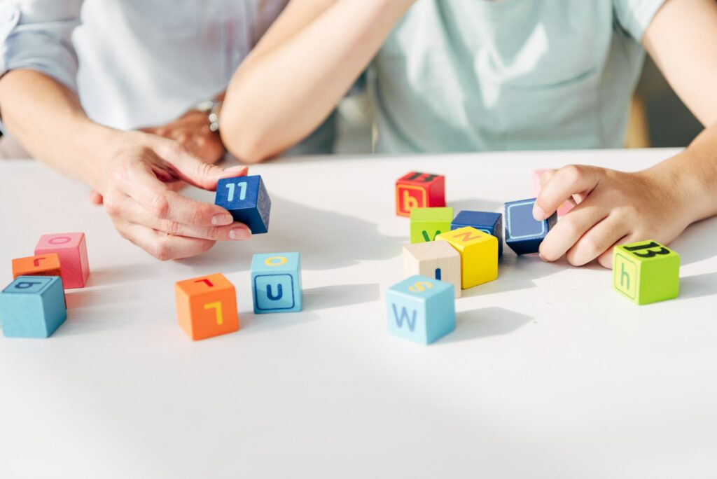 cropped view of child psychologist and kid with dyslexia playing with building blocks
