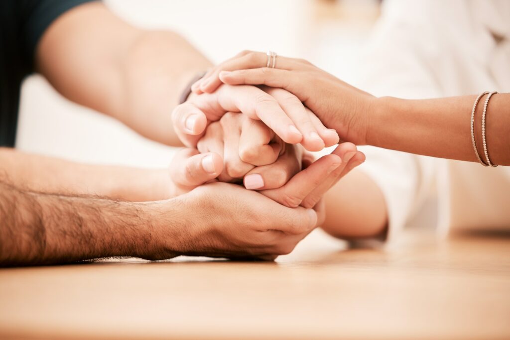 Support, care and family holding hands together at table to show empathy, love and hope. Closeup of