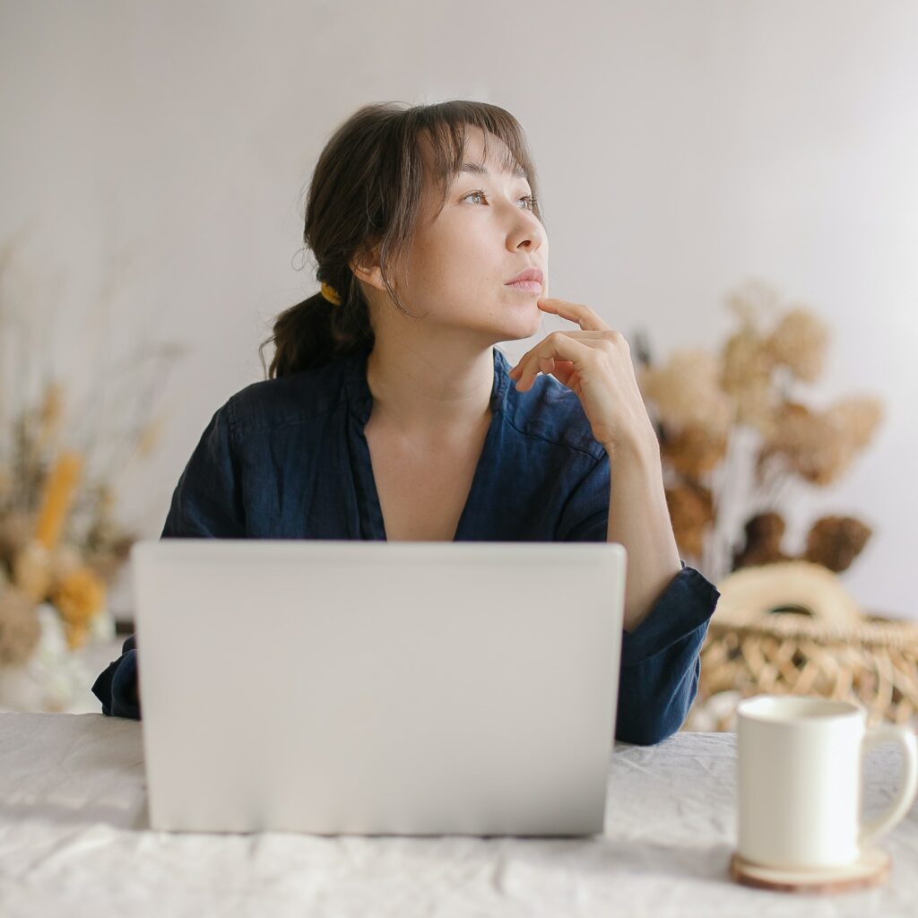 Young asian business woman looking aside and thinking about something while working from home